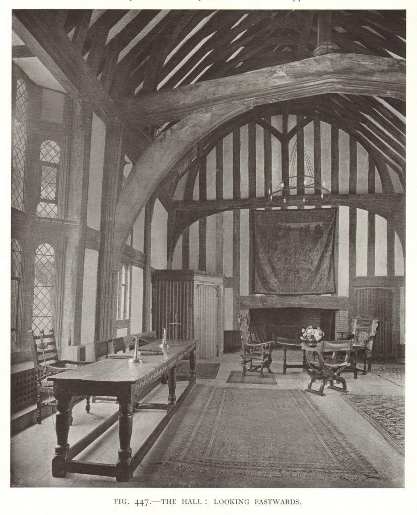 Black and white inmage showing the interior of a mediaeval hall, with period furniture